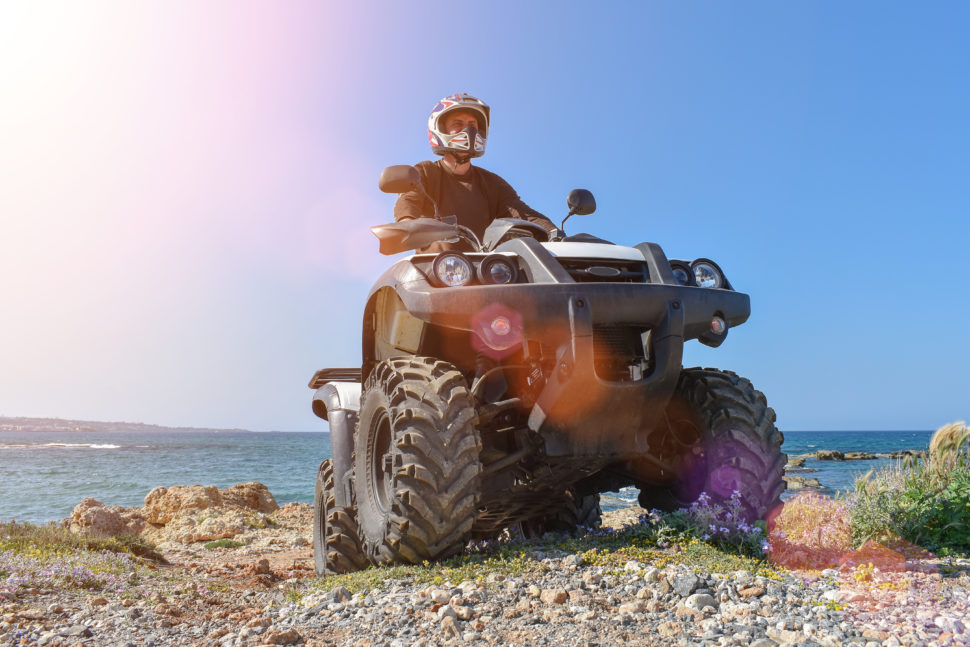 A man is driving an ATV on a beach.